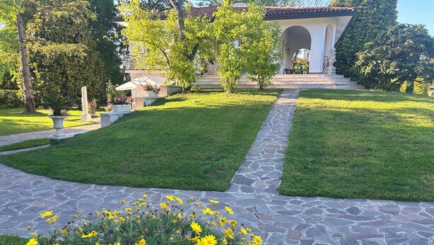 Un jardin bien entretenu, avec un chemin de pierre menant à un bâtiment doté d’un toit en tuiles et d’une entrée en arc de cercle.