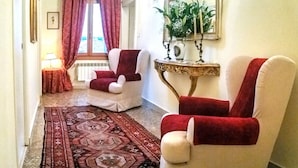 Un couloir avec un tapis à motifs, deux fauteuils, une petite table sur laquelle est posée une plante, et un miroir au mur.