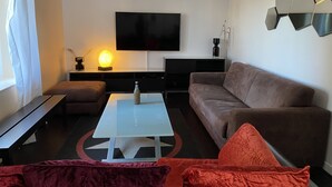 Een moderne woonkamer met een flatscreen televisie, een salontafel, een bank en een rode accentstoel.