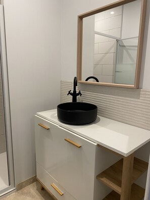 Een badkamer met een wit wastafelmeubel, een zwarte wastafel en een spiegel met houten omlijsting.