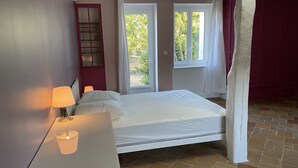 Een slaapkamer met een bed, nachtkastje, lamp, raam en deur.