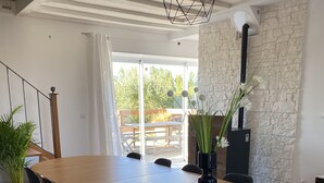 Een eetruimte met een lange houten tafel, zwarte stoelen, een potplant en een stenen muur.