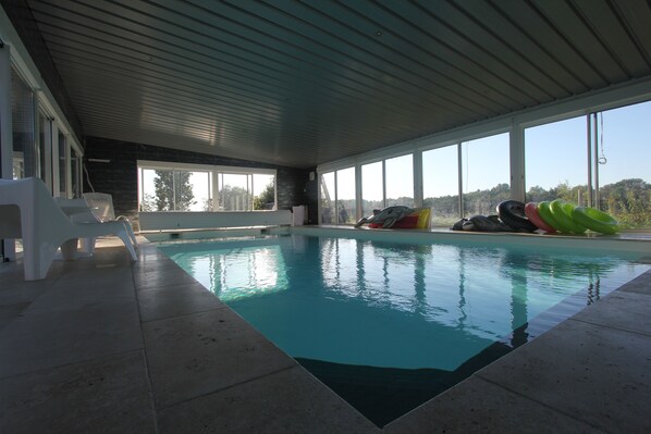 An indoor swimming pool with clear views through large windows, a tiled floor, and a ceiling with horizontal beams.