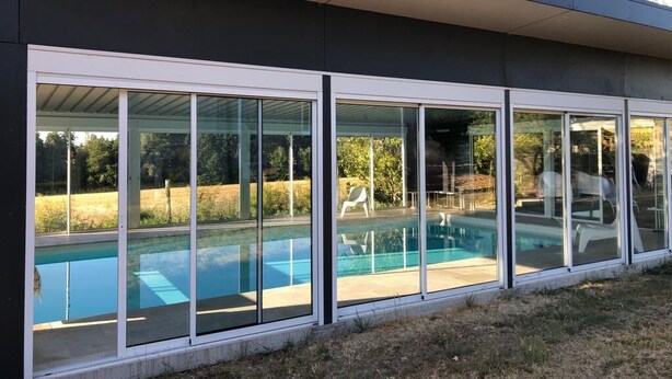 Een modern huis met een grote glazen deur die uitkomt op een zwembad.