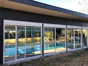 A modern house with a large glass door leading to a swimming pool area.