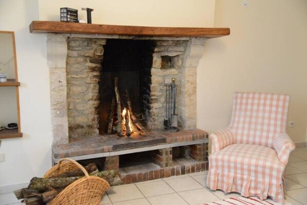 A fireplace with a stone surround, a wicker chair, and a checkered ottoman.