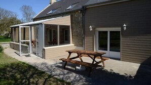 Et hus med en overdækket terrasse, et træbord og en stensokkel.