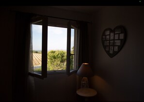 A room with a window overlooking a field, a wall-mounted heart-shaped decoration, and a table with a lamp. - Great House in the heart of the vineyard (Murviel-lès-Béziers)