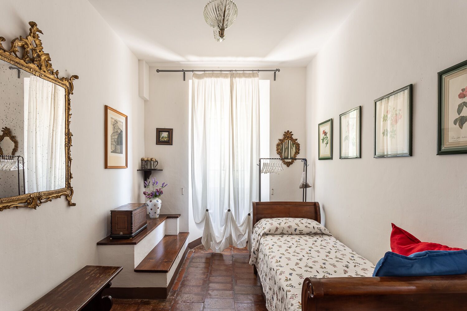 A bedroom with a bed, a wooden bench, a dresser, a mirror, and a chandelier.