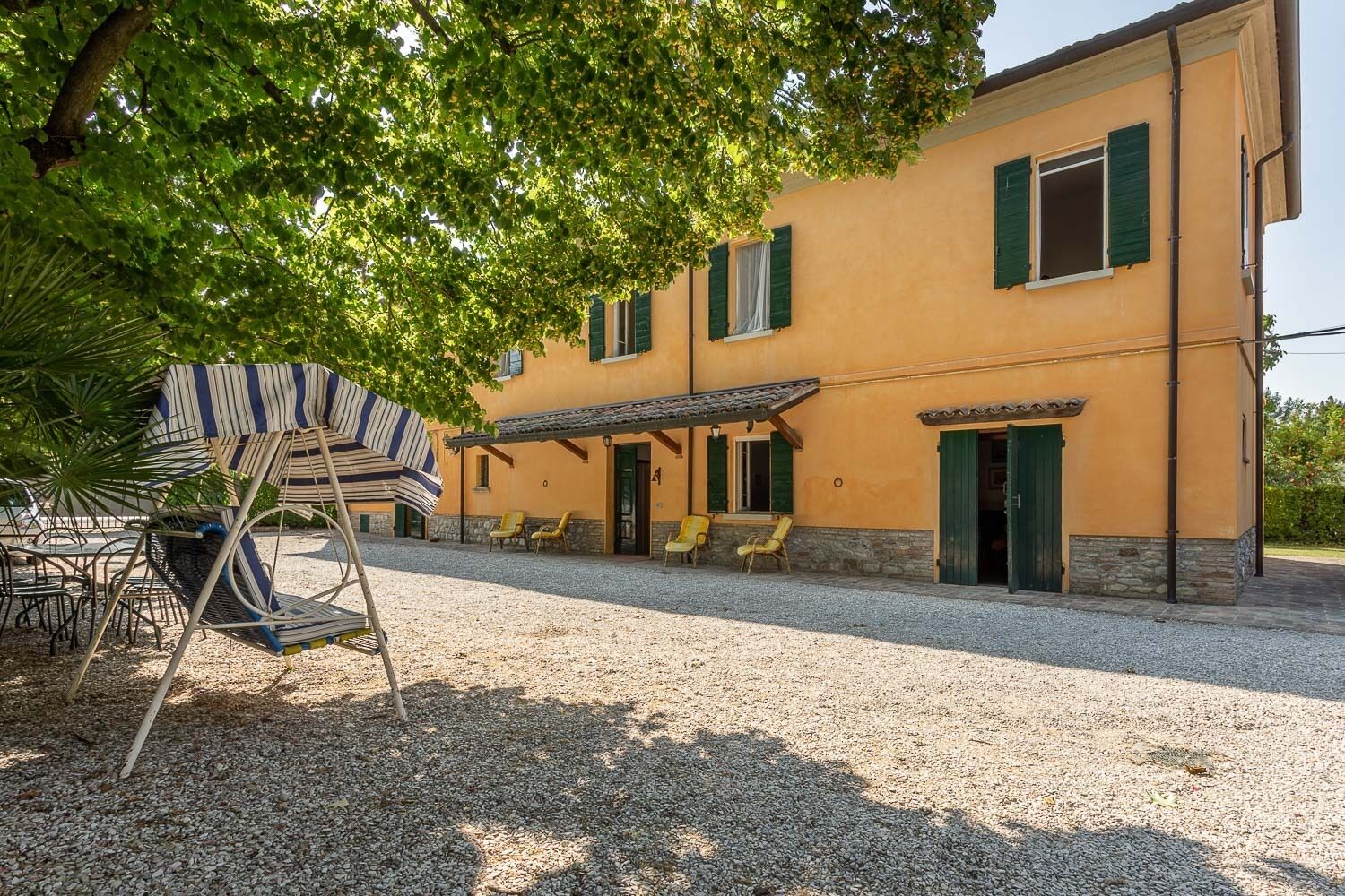 Un bâtiment avec une allée en gravier, un espace extérieur aménagé pour s’asseoir et une terrasse couverte.