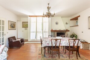 Comedor con una mesa dispuesta para seis personas, rodeada de sillas, una araña y una chimenea.