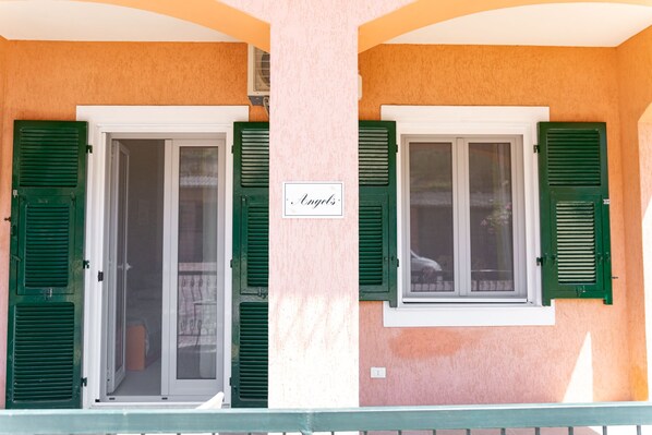 A building facade with two windows, each with green shutters, and a sign above the windows that reads "Angels".