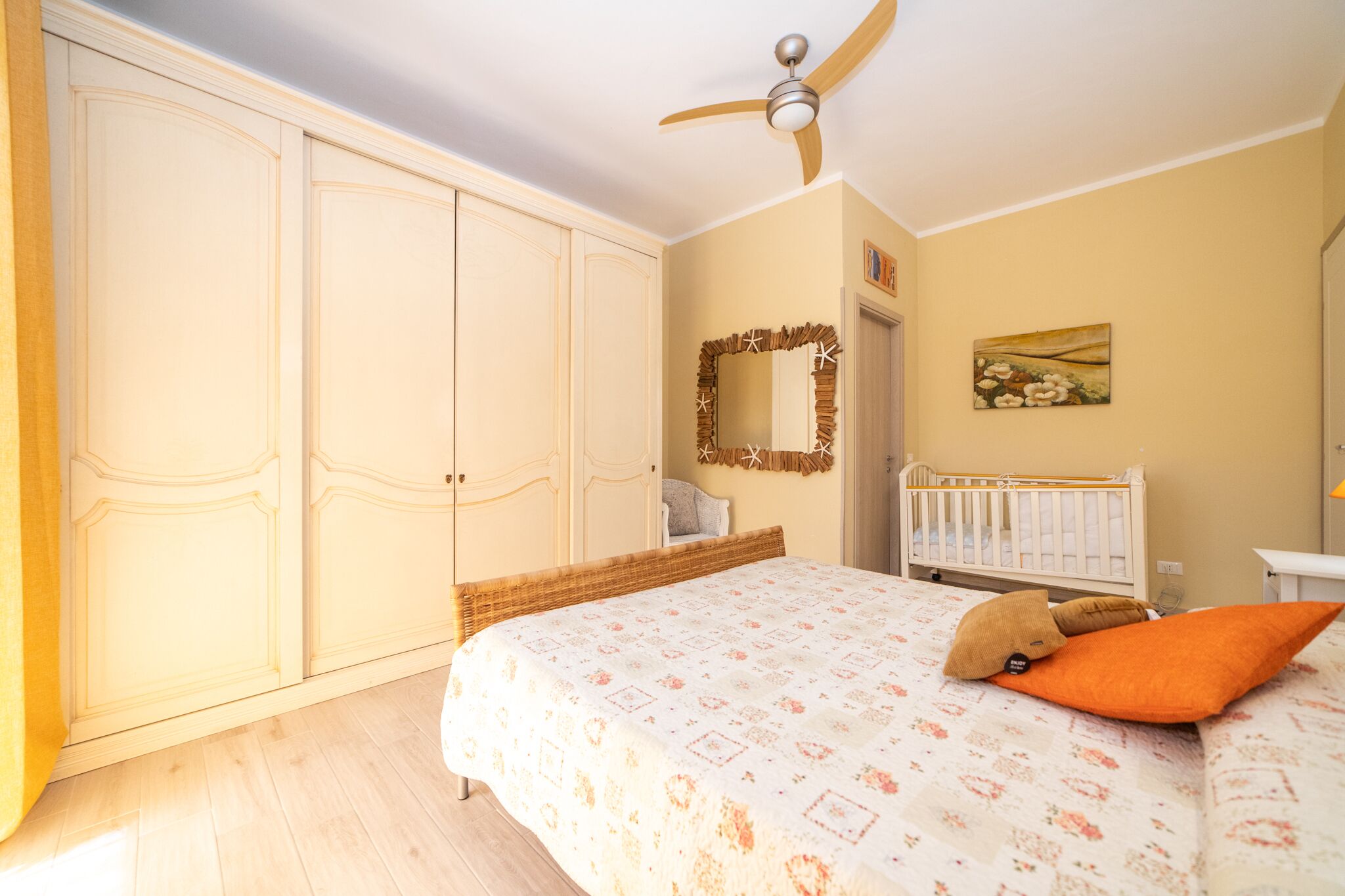 A bedroom with a bed, a ceiling fan, a crib, and a wardrobe.