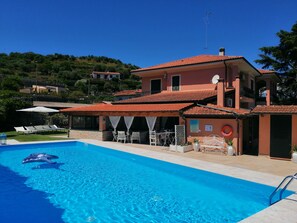 A two-story building with a swimming pool, outdoor seating, and a view of a hillside.