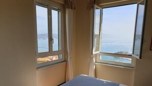 Une chambre d’hôtel avec un lit, deux serviettes et deux fenêtres donnant sur la mer et les bâtiments environnants.