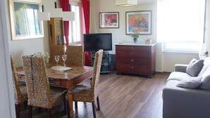 Un coin repas avec une table en bois et des chaises en osier, un téléviseur, une commode et un canapé.