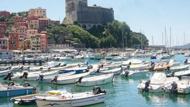 Un port de plaisance où sont amarrés de nombreux bateaux, un bâtiment historique en arrière-plan et des immeubles aux couleurs vives le long de la promenade.