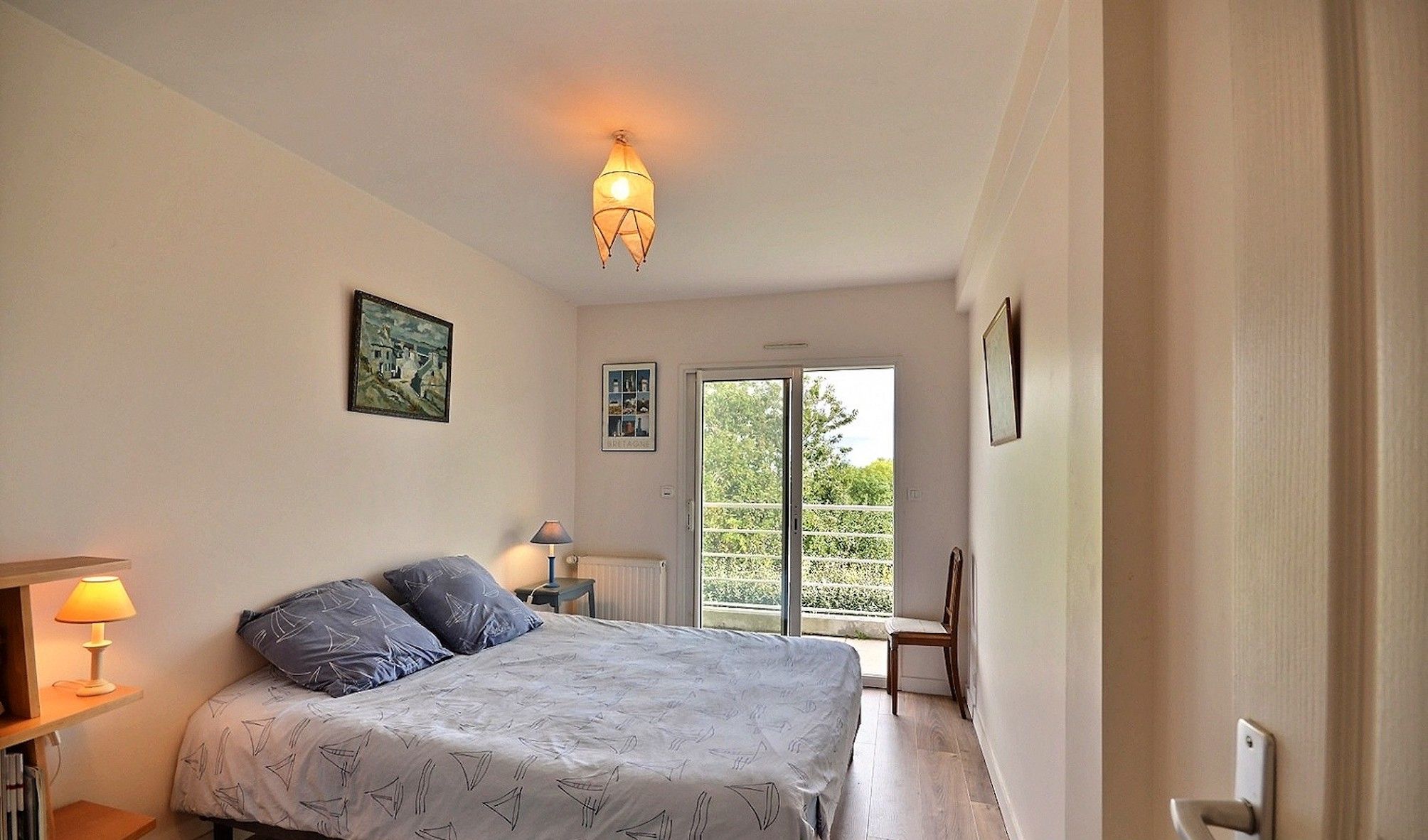 A bedroom with a bed, bedside lamps, a bookshelf, and a view through a sliding door to an outdoor balcony.