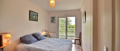 A bedroom with a bed, bedside lamps, a bookshelf, and a view through a sliding door to an outdoor balcony.