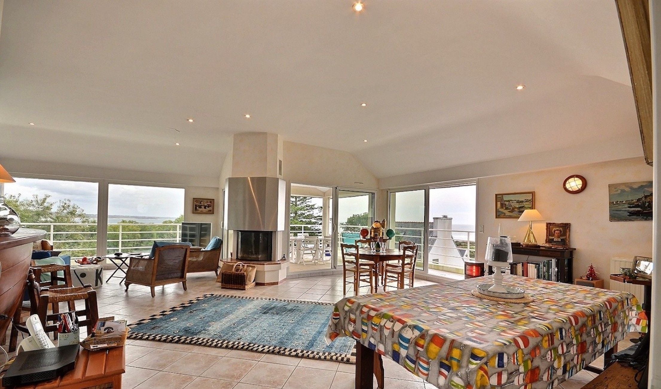 A spacious living area with a large dining table, comfortable seating, a fireplace, and large windows offering a view of the outdoors.