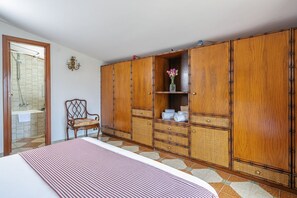 Une chambre à coucher comprenant un lit, une armoire en bois, une chaise et une salle de bain avec douche.