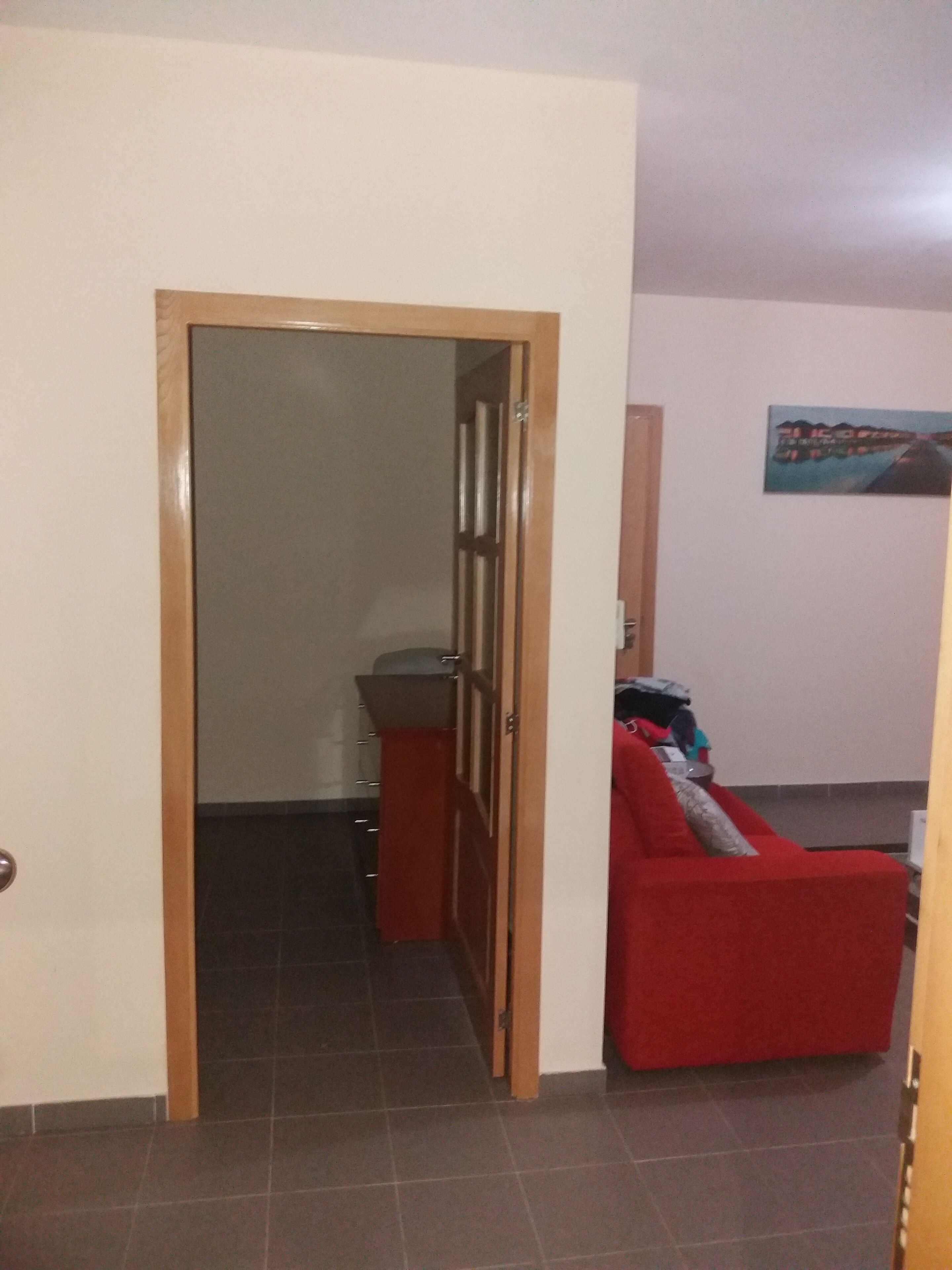 A hallway with a wooden door leading to a room with a red sofa and a small table.