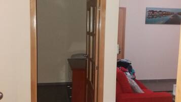 A hallway with a wooden door leading to a room with a red sofa and a small table.
