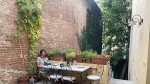 Una persona legge a un tavolo con piante in vaso e un muro di mattoni sullo sfondo.