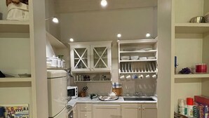 Una cucina compatta con mobili bianchi, un forno a microonde e un lavandino. Si vedono libri e utensili da cucina sugli scaffali.