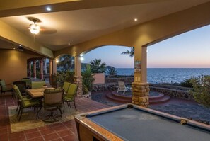 A pool table in a covered outdoor area with a view of the sea.