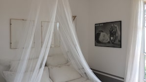 Un dormitorio con una cama bajo dosel, un cuadro en la pared y una ventana con cortinas.