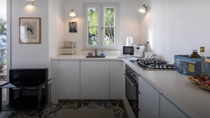 Cocina compacta con armarios blancos, estufa a gas, microondas y ventana con vista a vegetación.