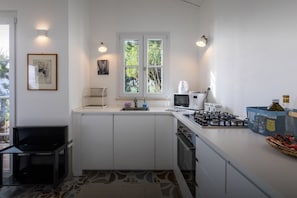 Une cuisine compacte avec des meubles blancs, une cuisinière à gaz, un four à micro-ondes et une fenêtre donnant sur un espace verdoyant.