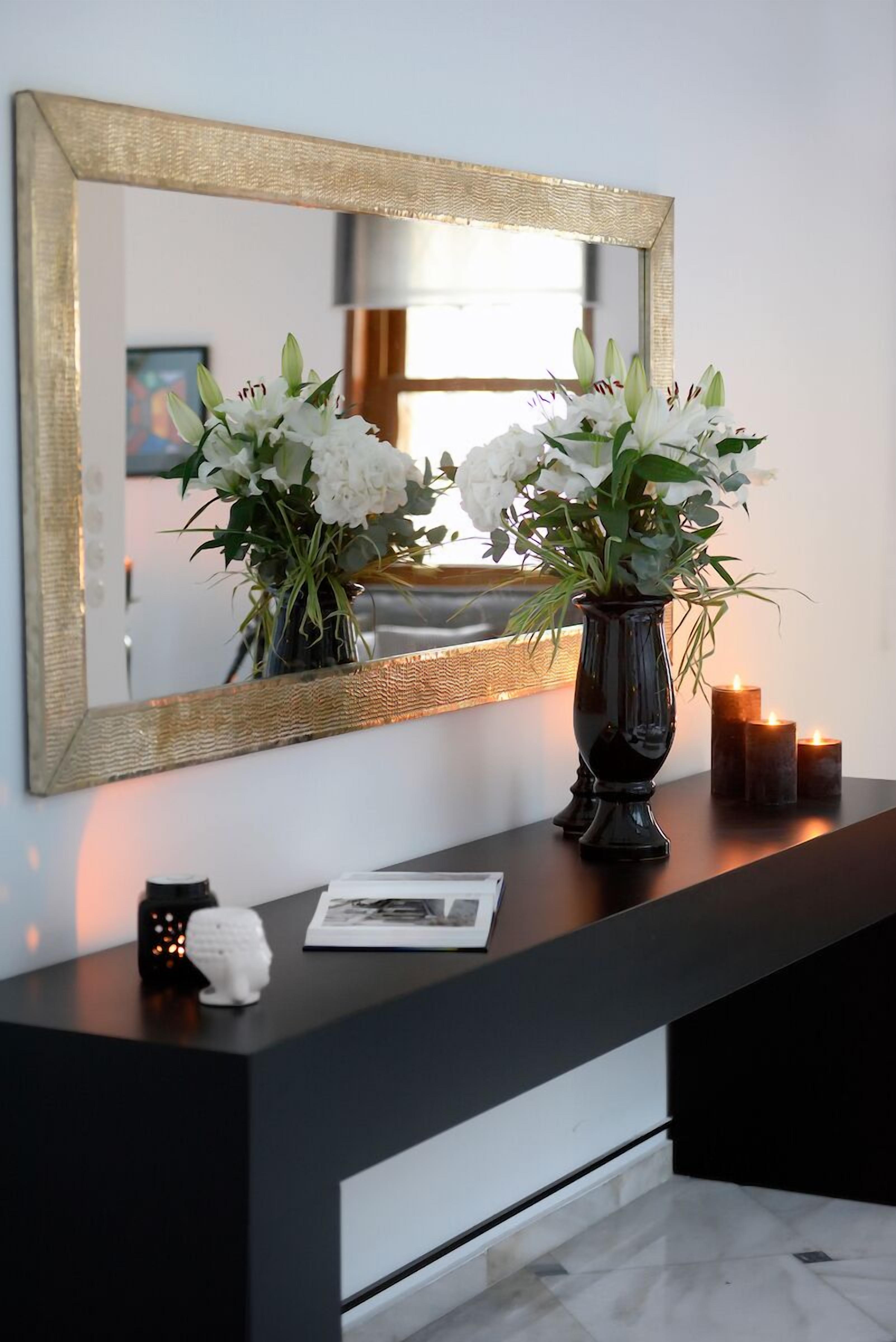 Un meuble-lavabo moderne avec un plan de toilette noir, un vase de fleurs blanches, un miroir avec un cadre doré et des bougies.