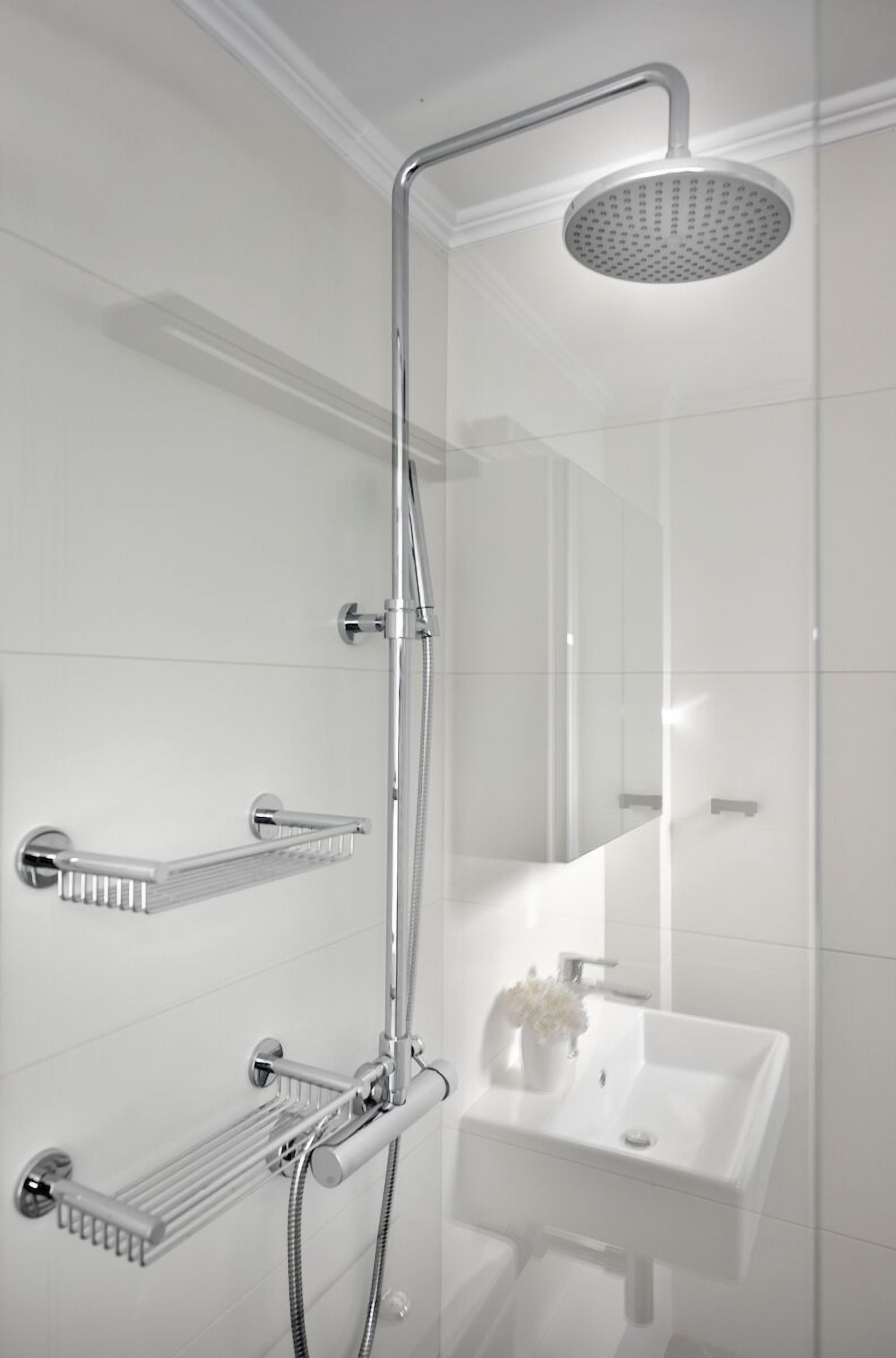 Une salle de bain moderne avec une douche à parois de verre, des robinetteries chromées et un lavabo apparent agrémenté d’un vase de fleurs.