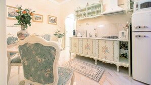 Zona pranzo con tavolo e sedie dal motivo floreale, un armadietto in stile vintage e un frigorifero.