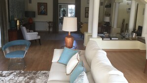 A spacious living room with a white sofa, a blue armchair, and a lamp. There is a dining area with a table and chairs in the background.