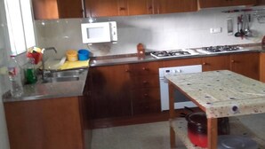 Una cocina con gabinetes de madera, un microondas, una estufa a gas, un fregadero y una mesa con una olla debajo.