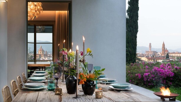 Une table à manger dressée pour six personnes, agrémentée de bougies, de fleurs et offrant une vue sur le paysage urbain.