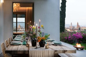 Une table à manger dressée pour six personnes, agrémentée de bougies, de fleurs et offrant une vue sur le paysage urbain.