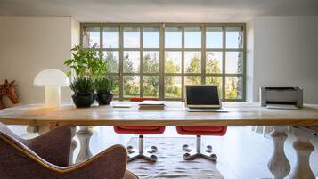 A room with a large window, a laptop, a printer, and two potted plants on a wooden table.