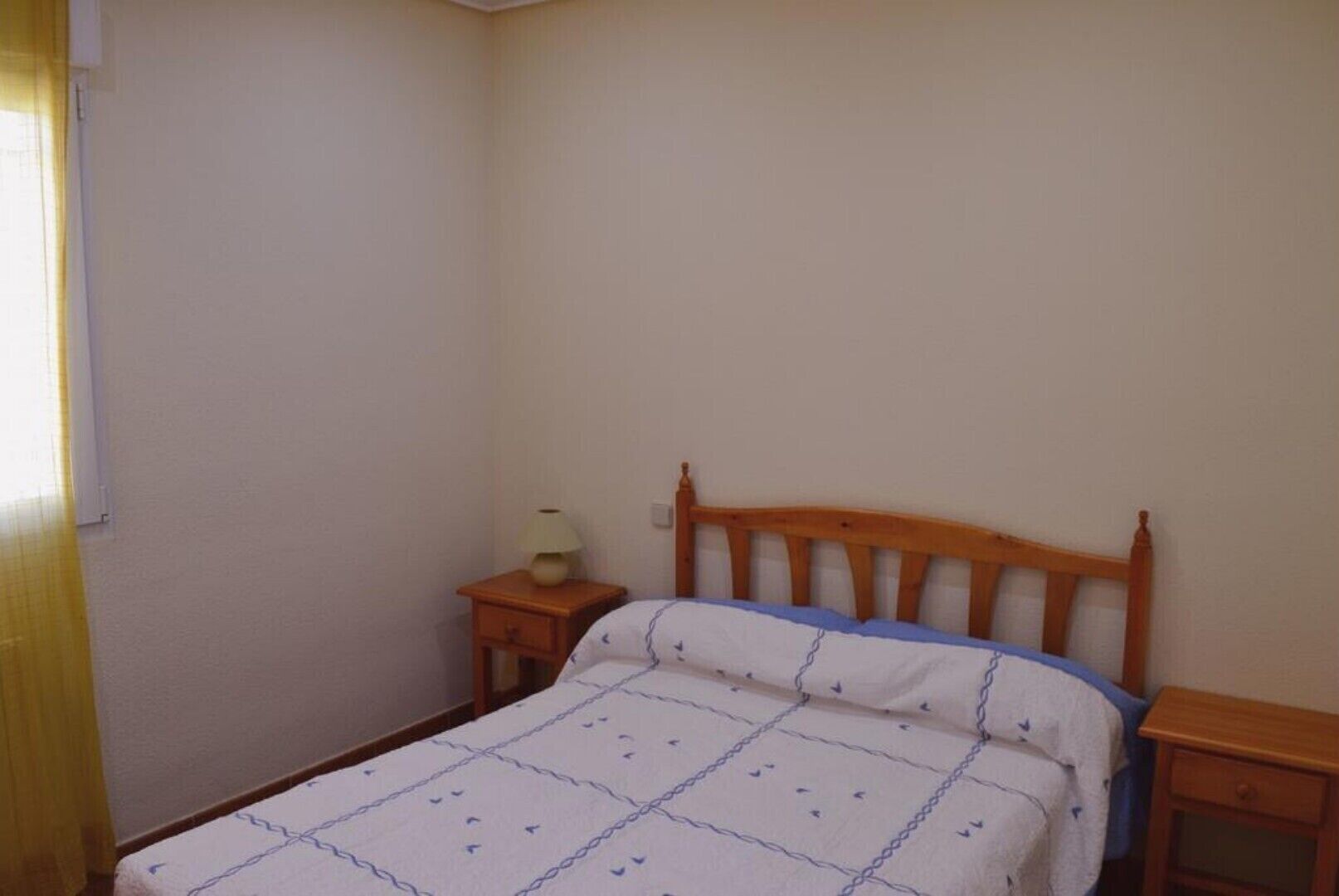 Une petite chambre simple, avec un lit simple, une table de chevet avec une lampe et une commode.