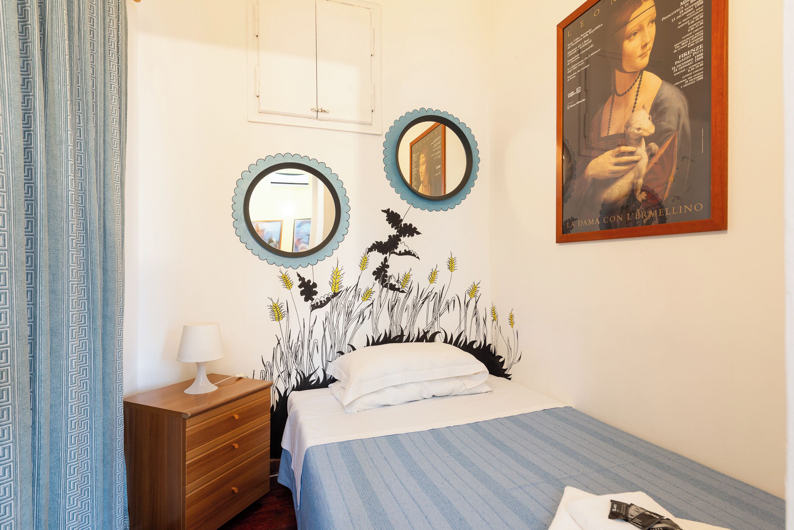 A bedroom with a bed, a dresser, two wall mirrors, and a framed painting.