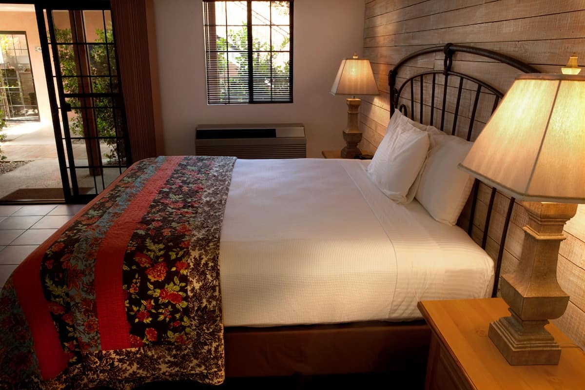 A neatly made bed with a floral bedspread, two bedside lamps, and a window with blinds.