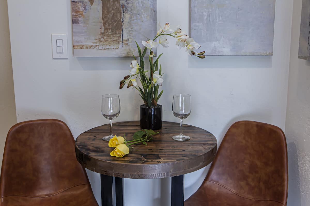 A round wooden table with two wine glasses and a vase with white flowers.
