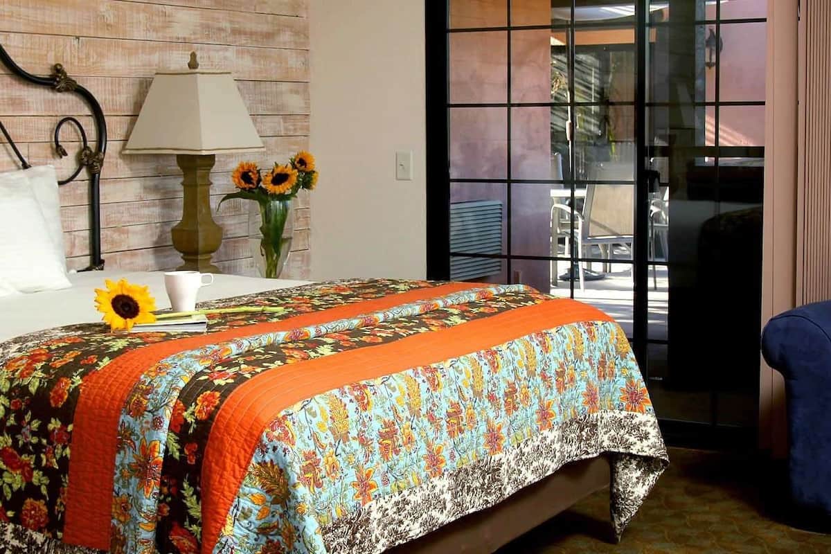 A bedroom with a bed, a blue armchair, a lamp, and a vase with sunflowers.