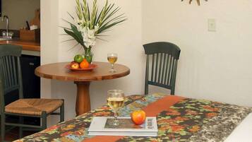 Ein Essbereich mit einem Tisch für zwei Personen, mit einer blumigen Tischdecke, einer Blumenvase und einem Teller mit Früchten und einem Weinglas.