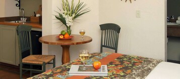 Ein Essbereich mit einem Tisch für zwei Personen, mit einer blumigen Tischdecke, einer Blumenvase und einem Teller mit Früchten und einem Weinglas.