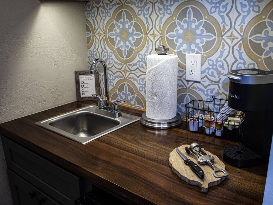 A kitchen with a stainless steel sink, a paper towel dispenser, a coffee maker, and a knife block on the counter.