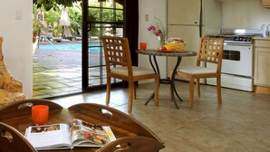 A living room with a sofa, two wooden chairs, a coffee table with a magazine, and a view of a pool and kitchen area. - Hotel California - A Town & Desert Boutique Hotel (Palm Springs)